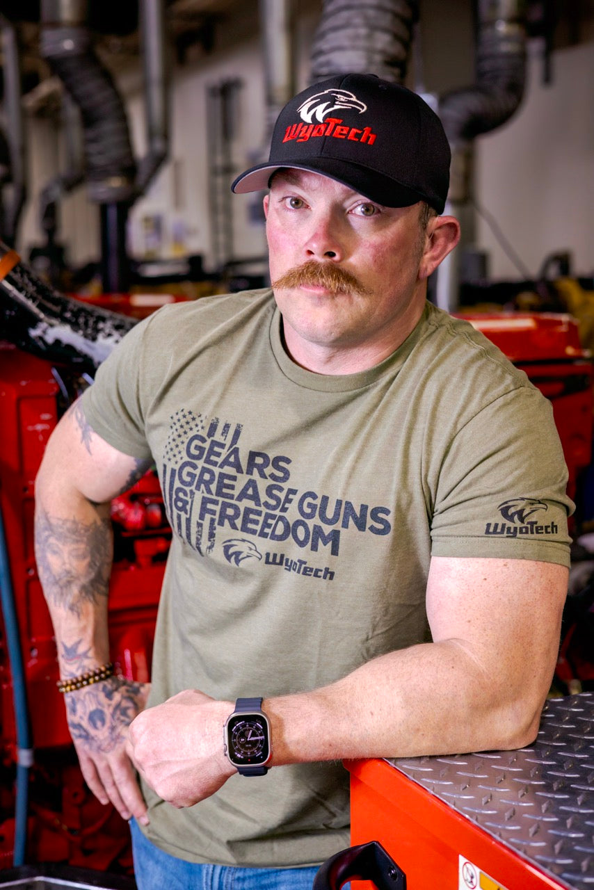 A man wearing a WyoTech T-Shirt that says "Gears Grease Guns & Freedom"